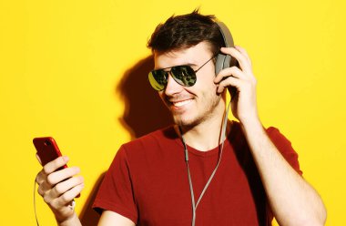 Kulaklık takan ve cep telefonu tutan genç bir adam..