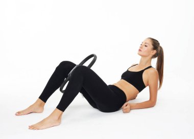 Mükemmel vücutlu genç bir kadın yerde oturuyor ve pilates yüzüğüyle antrenman yapıyor.