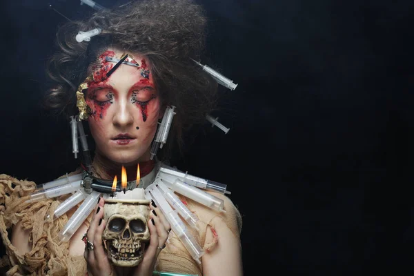 Mujer joven con maquillaje creativo y peinado sosteniendo una vela en un candelero de cráneo — Foto de Stock