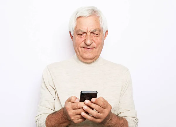 Senior man i casual outfit med modern smartphone och skrattar högt när du står på vit bakgrund. — Stockfoto