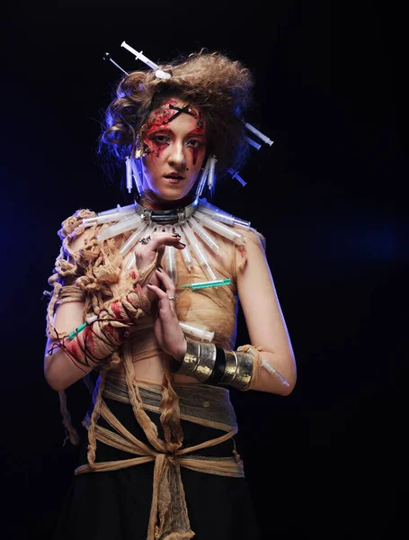 Una joven con un disfraz de zombi envuelta en vendajes y con jeringas en el pelo. — Foto de Stock