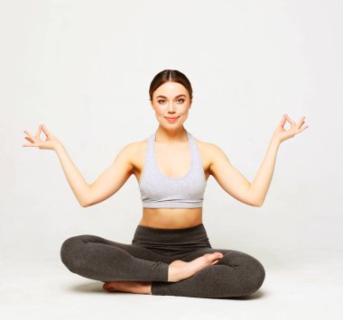 Yoga yapan, spor giyinen, beyaz arka planda çekim yapan genç bir kadın.