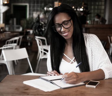 Yaşam tarzı ve insan konsepti: Güzel Afrikalı kız kafeteryada notlar alıyor