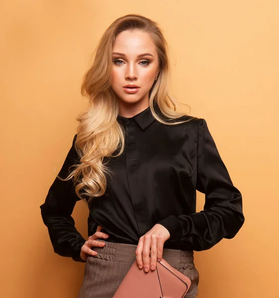 Young beautiful woman in a brown blouse and pants holds a handbag and posing on a beige background. — Stock Photo, Image