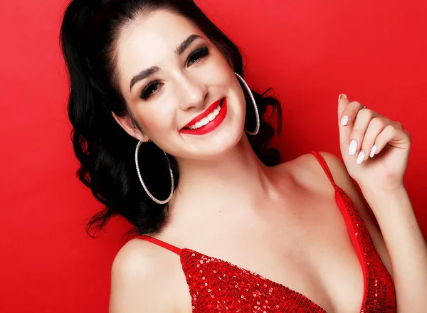 Lifestyle-, Party- und People-Konzept - Wunderschöne brünette Frau im Abendkleid kokett und verspielt auf rotem Hintergrund — Stockfoto