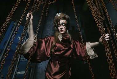 Parlak makyajlı bir kadın Steampunk sahnesinde ellerini kırmızı zincirlere uzatıyor..