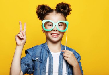 Parti, çocukluk ve insan konsepti: sarı arka planda kağıt karnaval aksesuarları olan küçük kız.