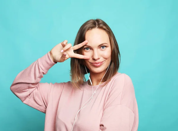 Portrait of a happy young blond female showing victory gesture and winking, studio shoot. — Stock Photo, Image
