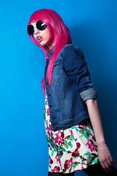 Young fashion female model with pink hair and big sunglasses over blue background — Stock Photo, Image