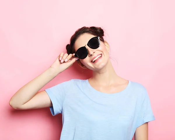Счастливое время. Молодая милая улыбающаяся брюнетка в повседневной синей рубашке и солнечных очках, позирующих на розовом фоне. — стоковое фото