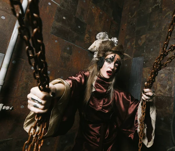 Γυναίκα με λαμπερό μακιγιάζ σε ένα σκηνικό steampunk κρατά με τα χέρια της για κόκκινες αλυσίδες. — Φωτογραφία Αρχείου