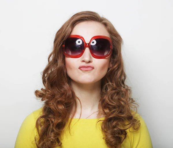 Hübsche junge lockige Frau mit gelbem Hemd und großer Sonnenbrille mit süßem Lächeln — Stockfoto