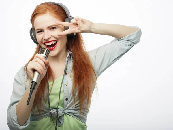 Mujer pelirroja joven cantando con un micrófono y auriculares, aislada sobre fondo blanco —  Fotos de Stock