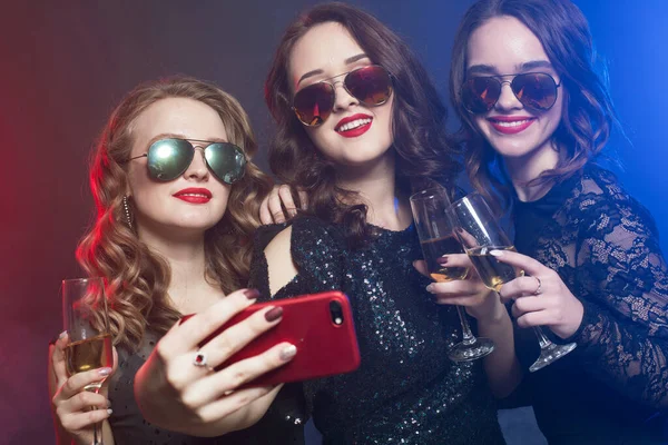 Modische junge Frauen in schwarzen Cocktailkleidern singen mit einem Mikrofon, halten Discokugeln, Sektgläser und lächeln — Stockfoto