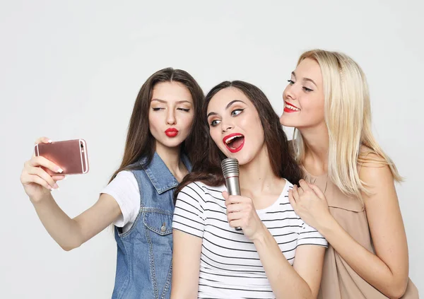 Lifestyle, emotion and people concept: three beauty girls with a microphone take selfie with smartphone — Stock Photo, Image