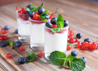 Doğal yoğurt, taze böğürtlen ve nane şekeriyle ahşap masada, yakın plan.