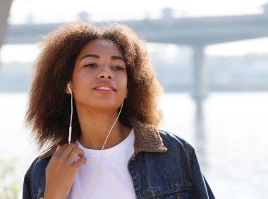 Büyüleyici afro-amerikalı genç bayan cep telefonuyla müzik dinliyor. Sıradan giyin..