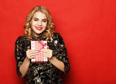 Yeni yıl, doğum günü, tatil konsepti: Kırmızı arka planda izole edilmiş hediye kutusunu tutan, gülümseyen genç bir kadının portresi