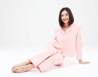 Pembe pijamalı güzel Asyalı kadın beyaz arka planda oturuyor.