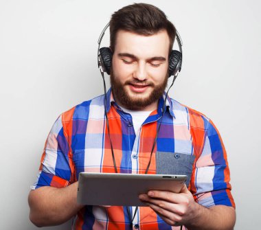 Açık gri arka planda kulaklık takan yakışıklı sakallı bir adamın stüdyo portresi..