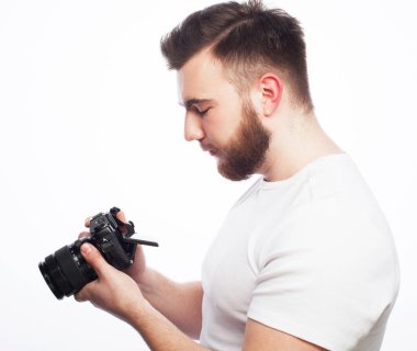 Genç sakallı fotoğrafçı beyaz arka plandaki kamera görüntülerine bakıyor.