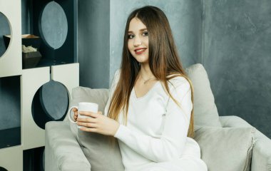 Takım elbiseli güzel sarışın kadın elinde bir fincan çay ya da kahve tutuyor.