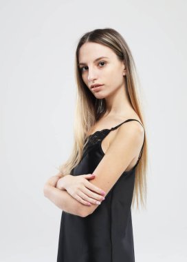 Siyah gecelikli güzel sarışın kadın beyaz arka planda poz veriyor.