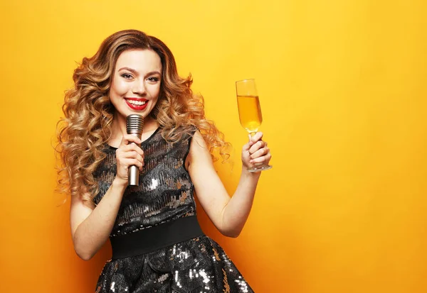Conceptul de petrecere și oameni: O tânără femeie de lux care poartă rochie de seară ținând pahar de șampanie și microfon . — Fotografie, imagine de stoc