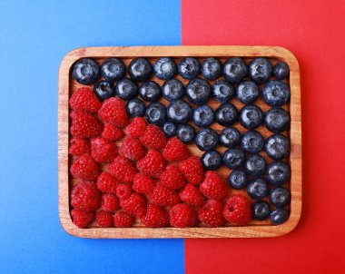 Ahşap tepside ahududu ve yaban mersini. Üst Manzara. Yakın plan. Mavi ve kırmızı arkaplan.