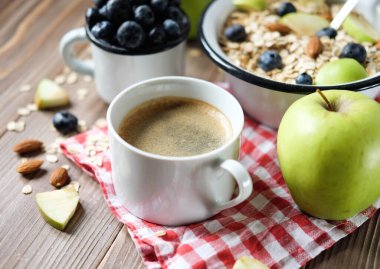 İyi günler dilerim. Sağlıklı bir kahvaltı yeni bir güne harika bir başlangıçtır. Tahta bir masada yulaf lapası, kahve, elma, böğürtlen ve fındık..