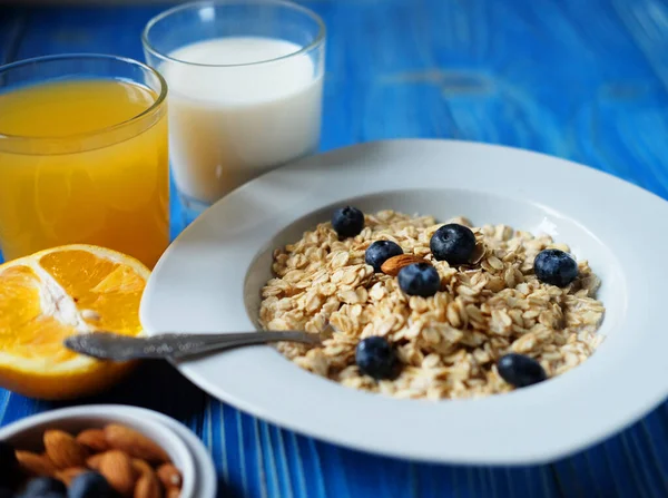 Healthy eating, food and diet concept - oatmeal with fresh berries on white plate with orange juice and milk, blue wooden background.
