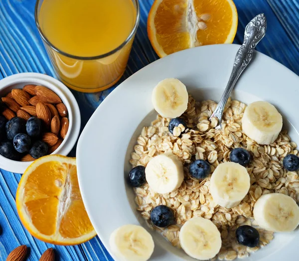 Beyaz tabakta taze böğürtlen ve mavi ahşap arka planda portakal suyu bulunan yulaf ezmesi..
