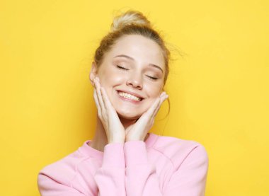 Çekici sarışın gülüyor ve hayattan zevk alıyor. Sarı arka planda pembe kazak giymiş bir kız. Mutluluk ve duygu kavramı.