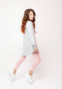 Uzun kıvırcık saçlı, beyaz arka planda gelişigüzel poz veren küçük kız.