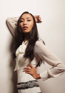 Uzun saçlı, beyaz arka planda şık beyaz elbiseli güzel Asyalı kadın modeli.