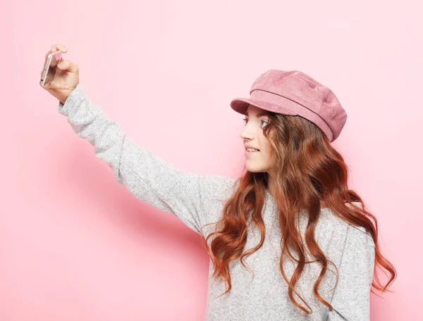 Портрет веселой маленькой девочки в шляпе, делающей селфи на розовом фоне — стоковое фото