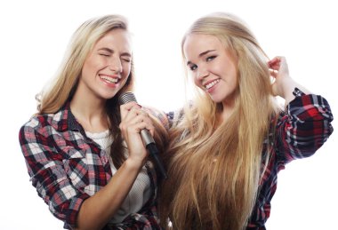 İki genç kız arkadaş birlikte duruyor ve beyaz arka planda gülümsüyor..