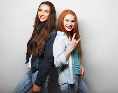 İki genç kız arkadaş birlikte duruyor ve beyaz arka planda gülümsüyor..