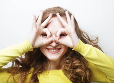 Neşeli kıvırcık kadın sıfıra bakar ya da tamam, yuvarlak parmaklarını gözüne yakın tutar.