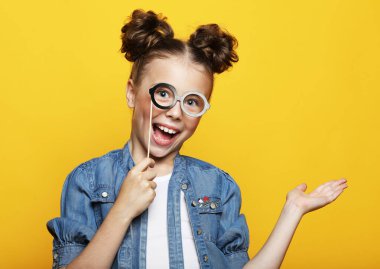 Parti, çocukluk ve insan konsepti: sarı arka planda kağıt karnaval aksesuarları olan küçük kız.