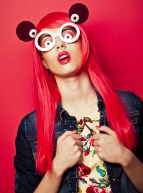 Pembe saçlı, pembe arka planda büyük güneş gözlüklü, modaya uygun genç bir kadın.