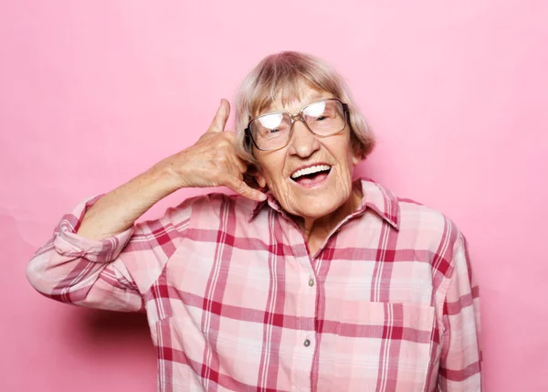 Ηλικιωμένη γυναίκα φορώντας ροζ πουκάμισο στέκεται πάνω από ροζ φόντο χαμογελώντας κάνει τηλεφωνική χειρονομία με το χέρι και τα δάχτυλα σαν να μιλάμε στο τηλέφωνο. — Φωτογραφία Αρχείου