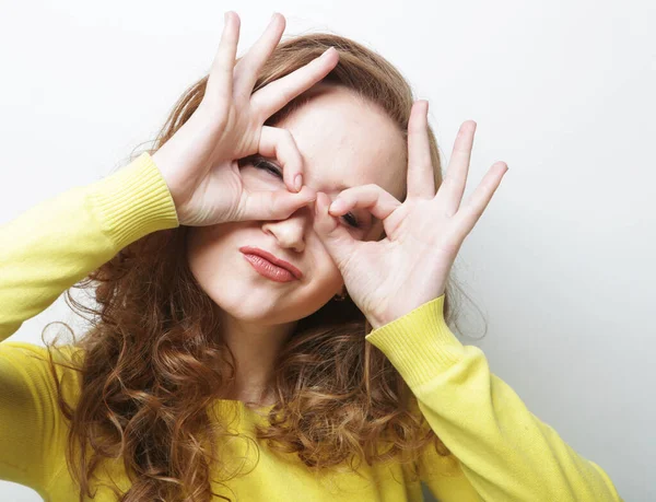Mujer rizada alegre mira a través de cero o gesto ok, sostiene los dedos redondeados cerca del ojo —  Fotos de Stock