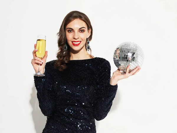 Dovolená, lidé a oslavit koncept: Krásná brunetka žena ve večerních šatech, elegantní účesy a make-up drží disco koule a sklenice se šampaňským. — Stock fotografie