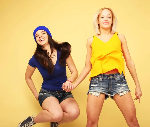 Sarı arka planda birlikte atlayıp gülen iki genç kadın. — Stok fotoğraf