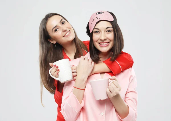 Kırmızı ve pembe pijamalı iki güzel genç bayan kahve bardaklarını tutuyorlar. — Stok fotoğraf