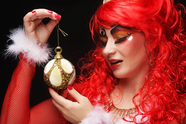 Όμορφη νεαρή γυναίκα με καλλιτεχνικό μακιγιάζ και κόκκινη περούκα κρατώντας μπάλες Χριστουγέννων. — Φωτογραφία Αρχείου