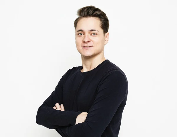 Young handsome man wearing black sweater crossing hands and look at camera over white background — Stock Photo, Image