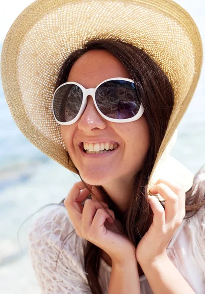 Glad kvinna bär sommar vit klänning, hatt och solglasögon på stranden. — Stockfoto
