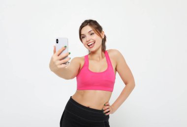 Akıllı telefonlu gülümseyen bir fitness kadınının portresi. Selfie zamanı. beyaz arkaplan